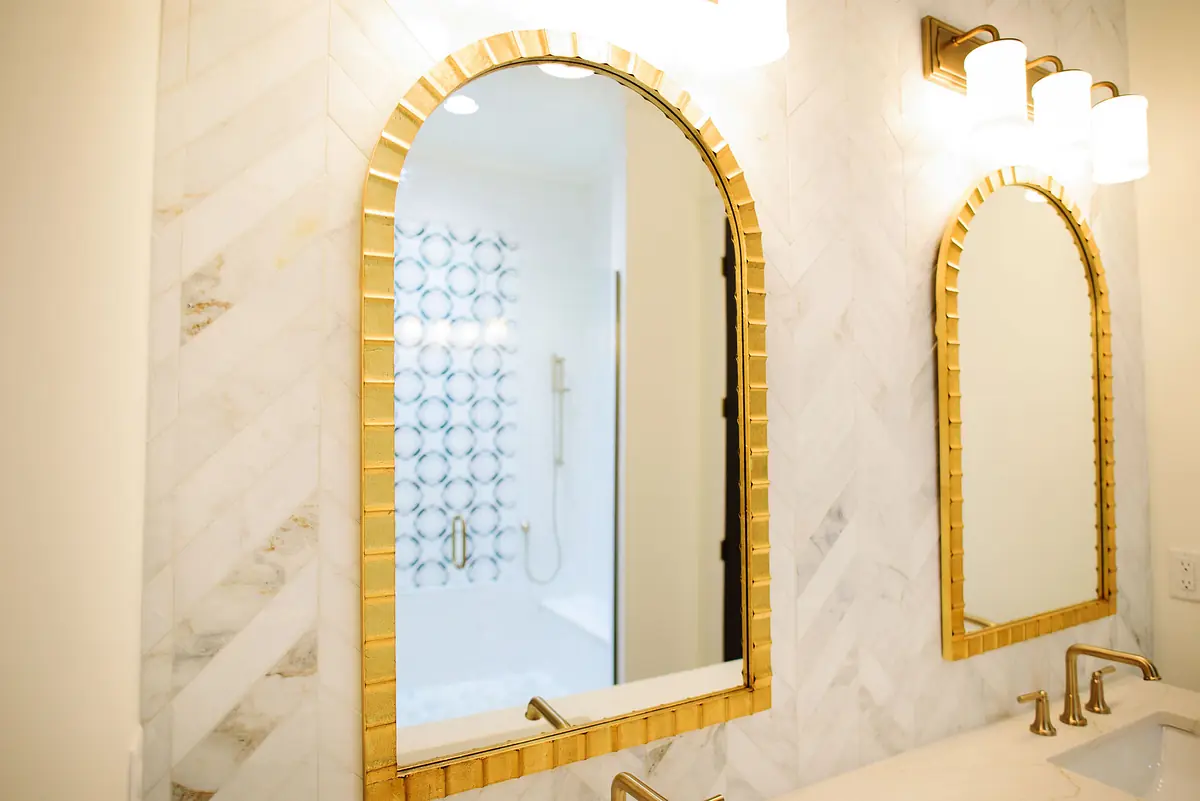 Bathroom with dual gold-framed mirrors, marble countertop, installed faucets, and a patterned shower curtain