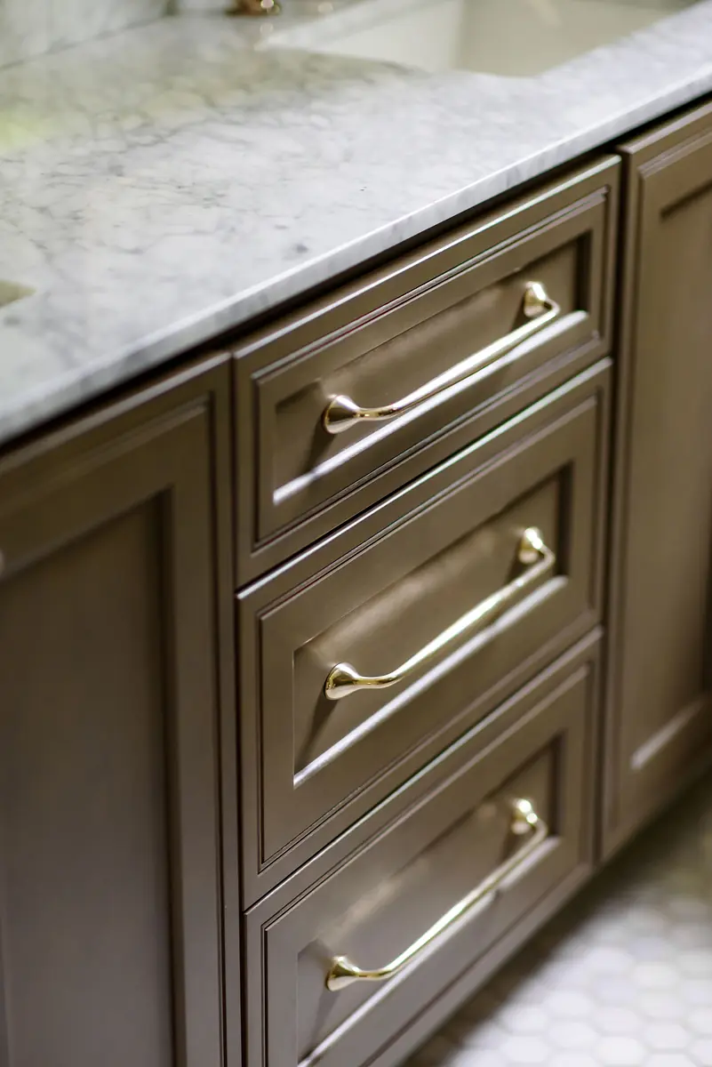 Bathroom vanity with marble countertop, gray cabinetry, gold handles, and geometric tile flooring
