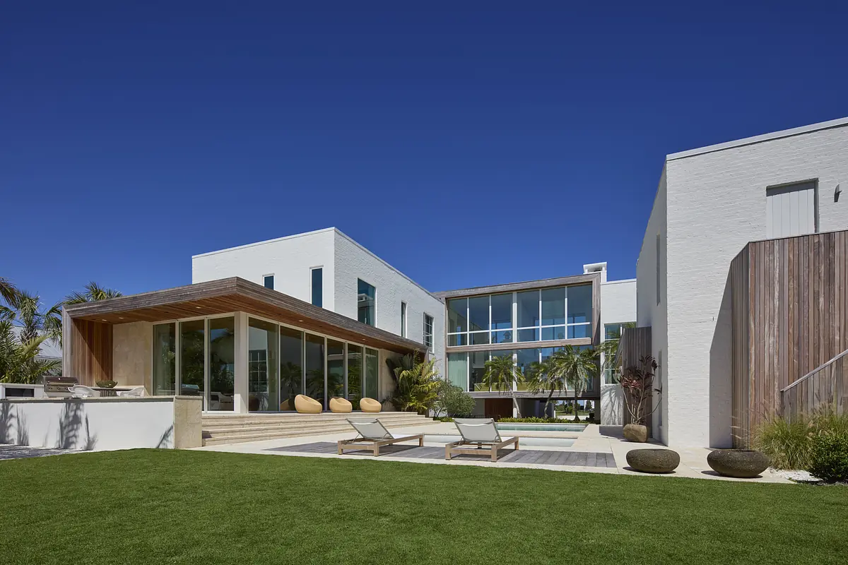 Modern exterior rear view with flat roof, glass windows, wooden deck, loungers, pool, and landscaping.