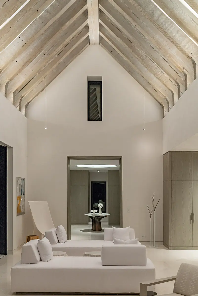 Living room with white sofas, light coffee table, area rug, wooden beams, and decorative sculpture in the corner