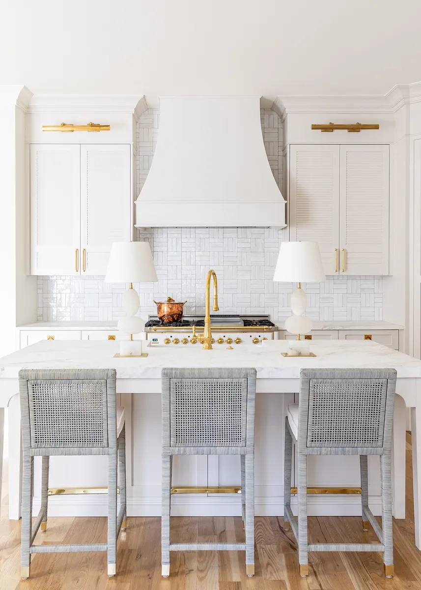 Kitchen with white marble island, gray wicker seats, range hood, and textured tile backsplash.