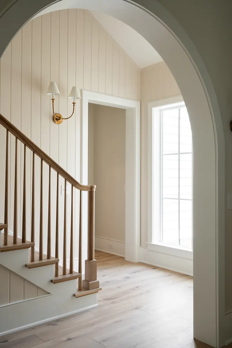 Foyer with staircase, beige walls, large window, and wall sconce.