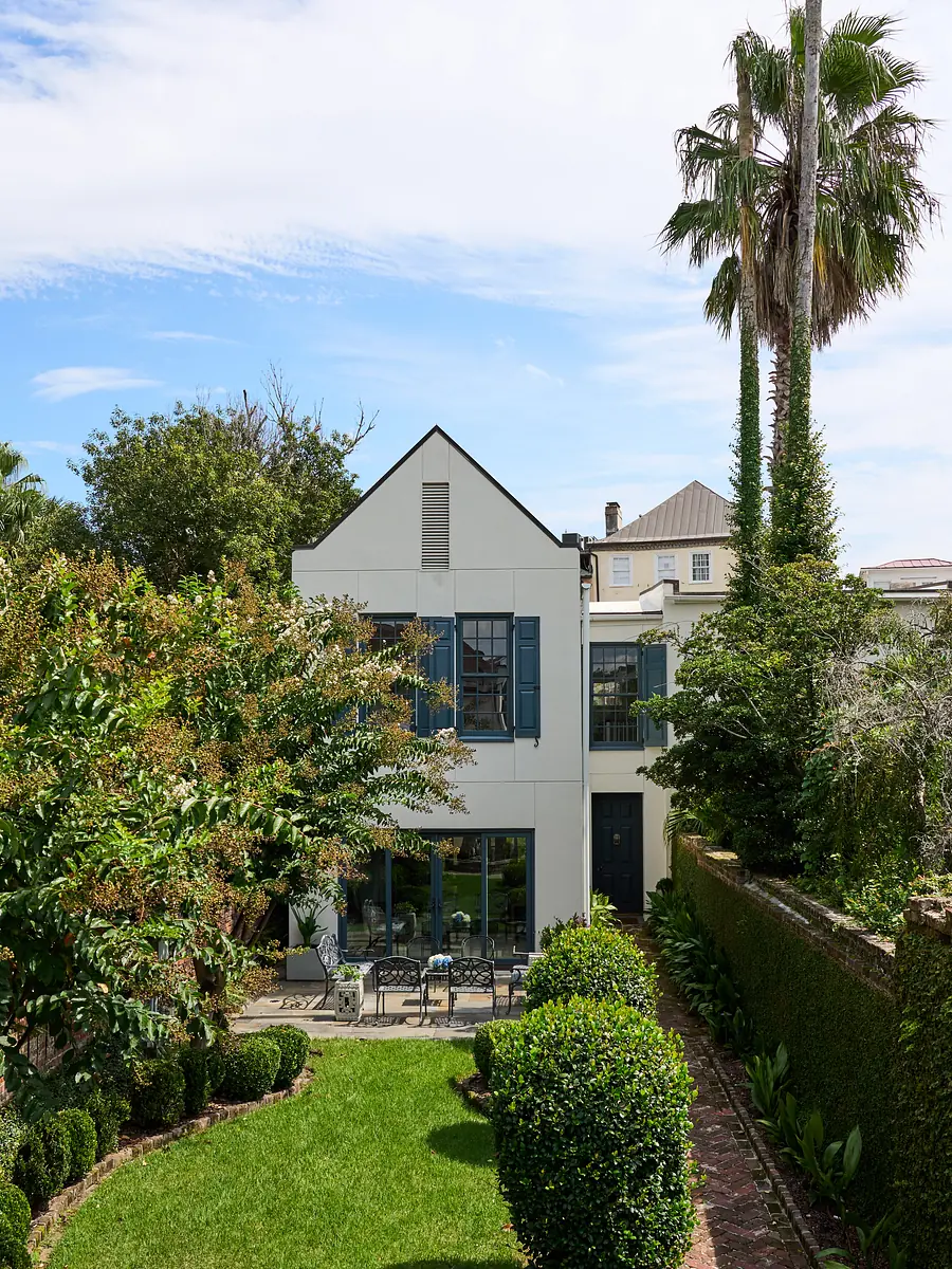 Rear exterior view of two-story house with large windows, porch, gardens, and palm trees.