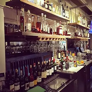 Bar area with long countertop, shelves of liquor bottles, and hanging glasses.