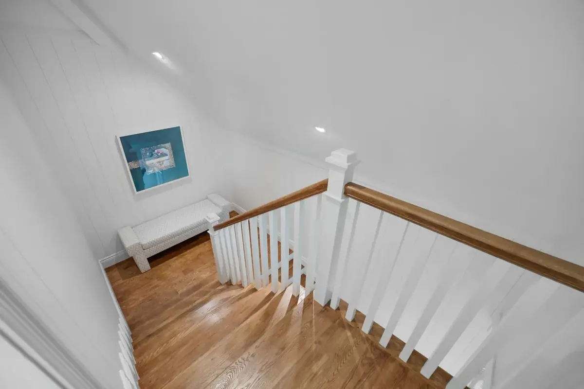 Hallway with wooden flooring, white walls, white bench, artwork, and recessed lighting