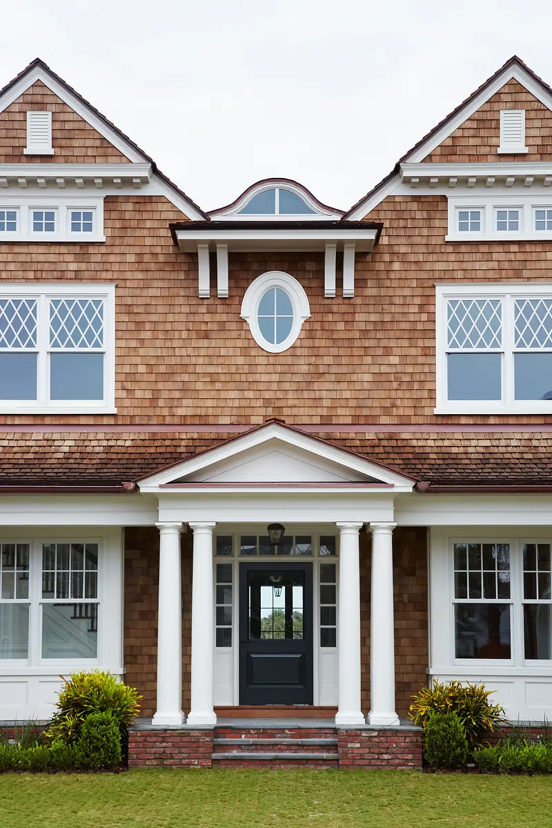 Exterior front of a house with shingle siding, gabled roofs, columns, and a central entrance.