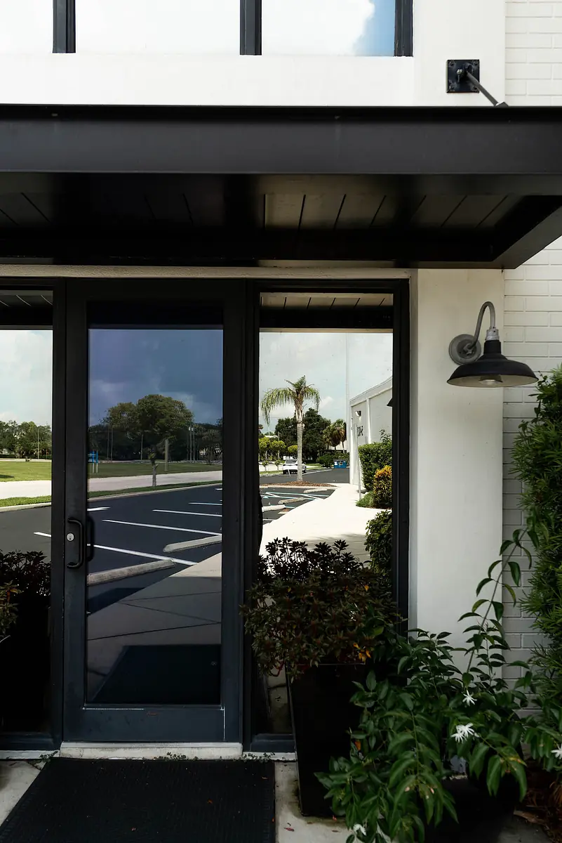 Exterior front with black front door, large windows, and planters with greenery.