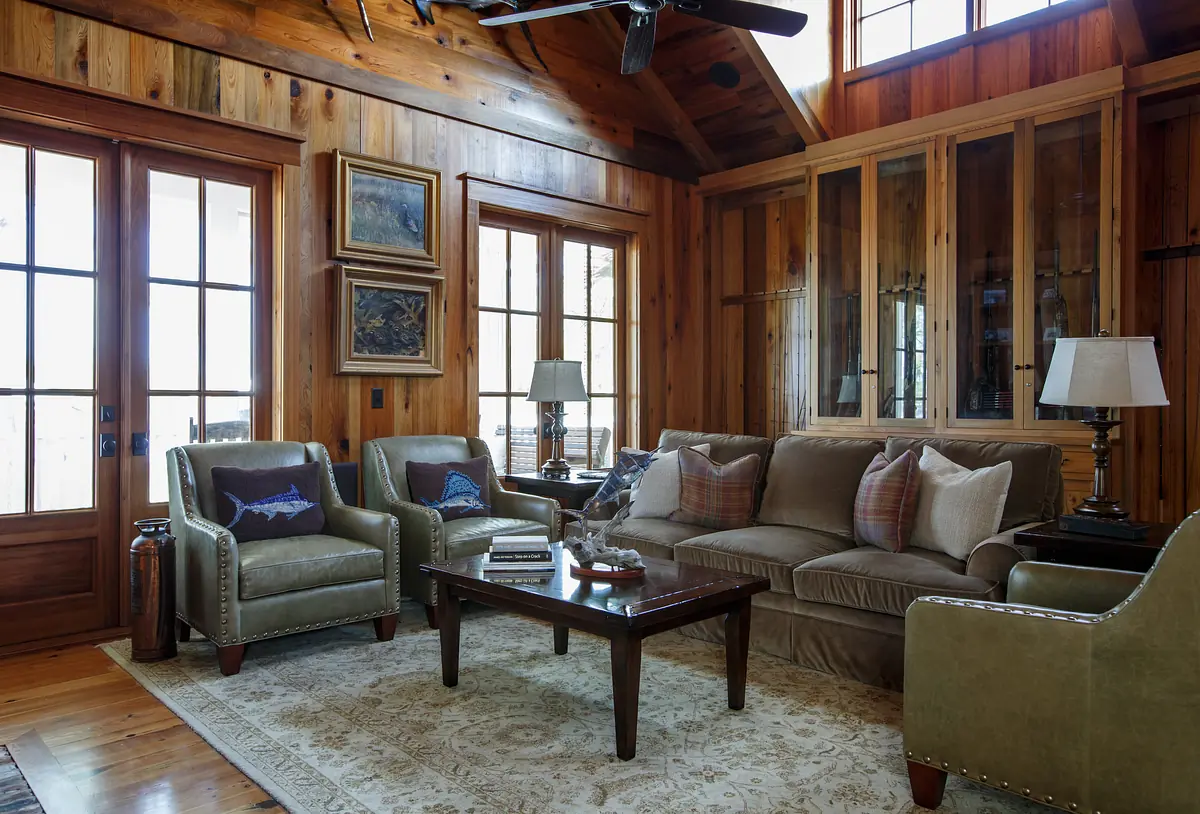 Living room with tan sofa, green armchairs, dark wood coffee table, area rug, and large windows with wooden trim
