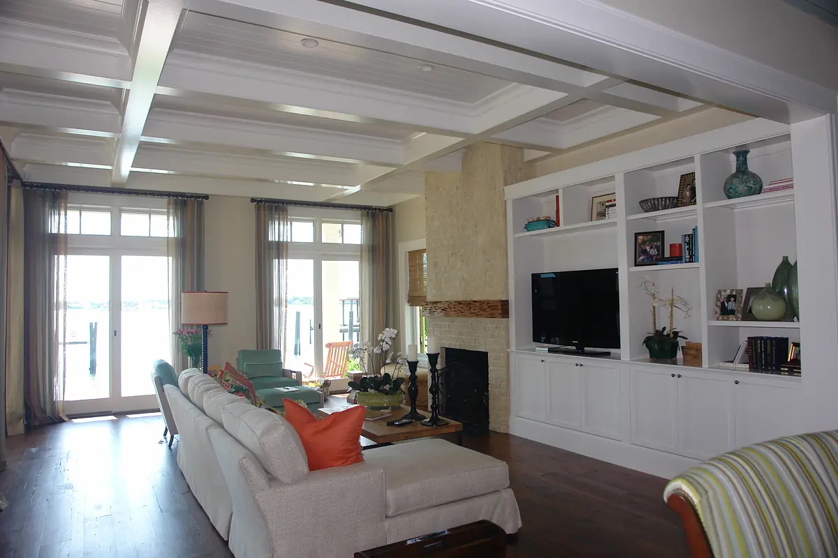 Living room with white sofa, wooden coffee table, green chairs, stone fireplace, and large windows.
