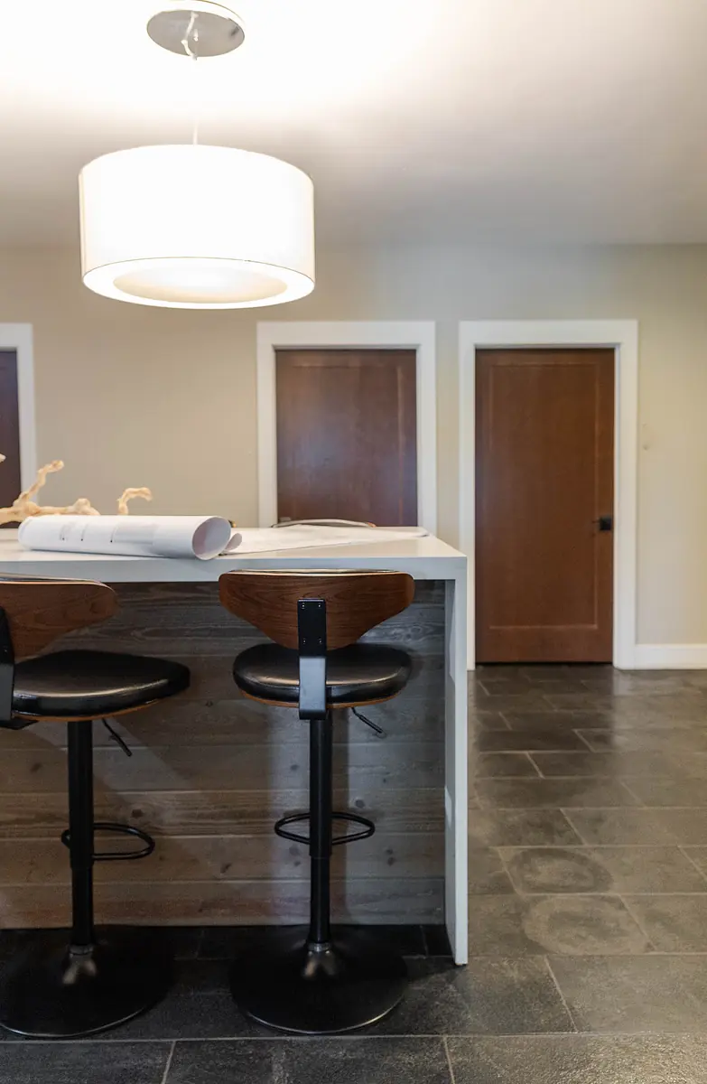 Kitchen with bar counter, black and wood stools, dark tiles, and two doorways.