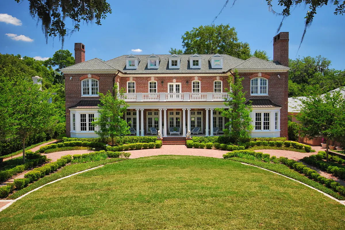 Exterior front of a large brick house with a porch, landscaped yard, and brick pathway.