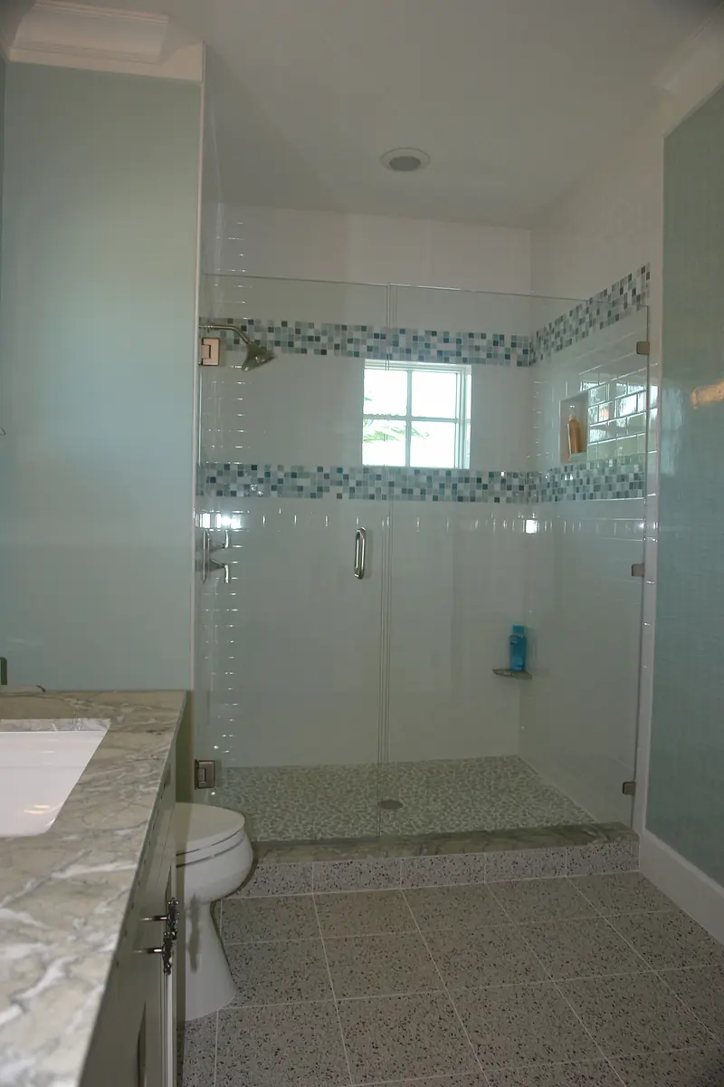 Bathroom with glass shower enclosure, tiled floor, white toilet, marble countertop, and light green walls.
