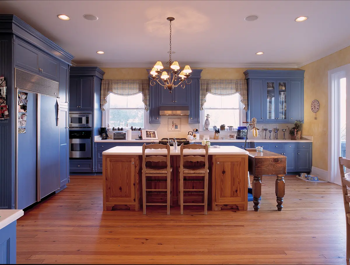 Kitchen with blue cabinetry, center island, wooden stools, stainless steel appliances, and large windows.