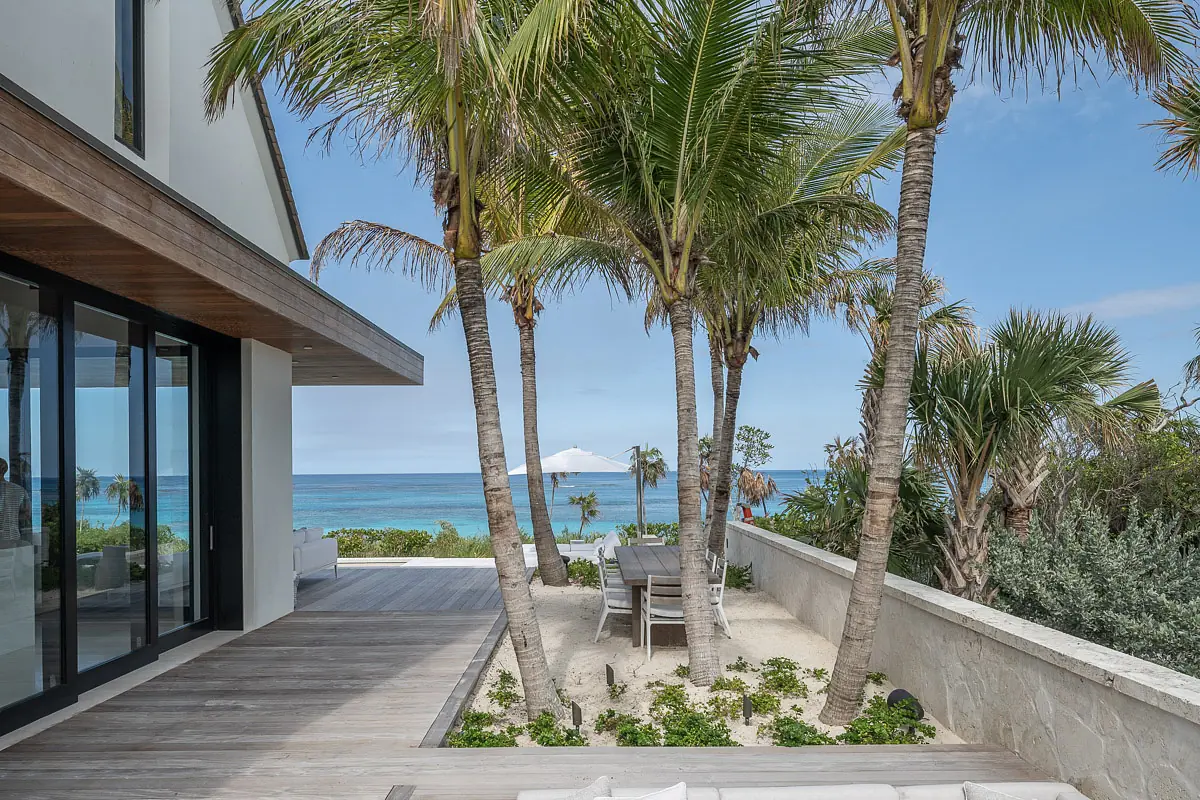 Outdoor patio with wooden decking, dining table, chairs, palm trees, and ocean view.