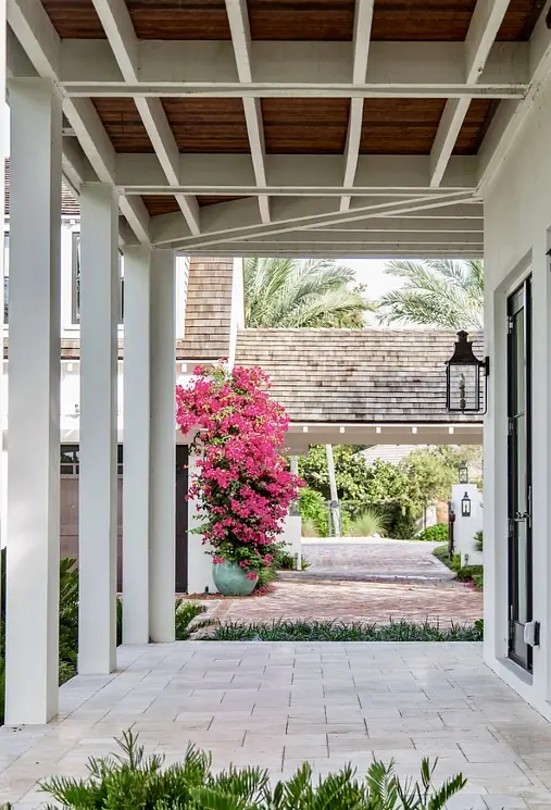 Exterior front area with covered porch, white columns, stone flooring, bougainvillea plants, and brick pathway.