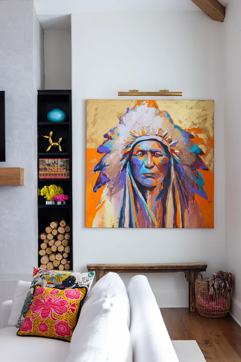 Living room with white sofa, colorful cushions, artwork, wooden bench, and black shelving unit.