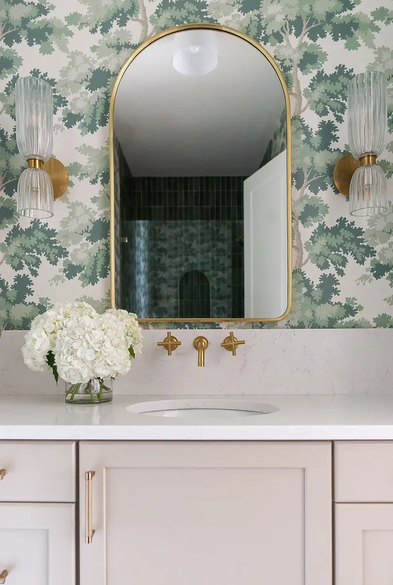Powder room with mirror, wall sconces, marble countertop, floral wallpaper, and floral arrangement