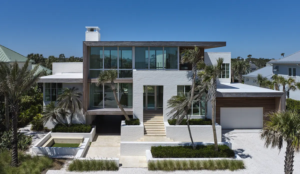 Modern residence with white exterior, large glass panels, wooden accent wall, stairs, and palm trees.