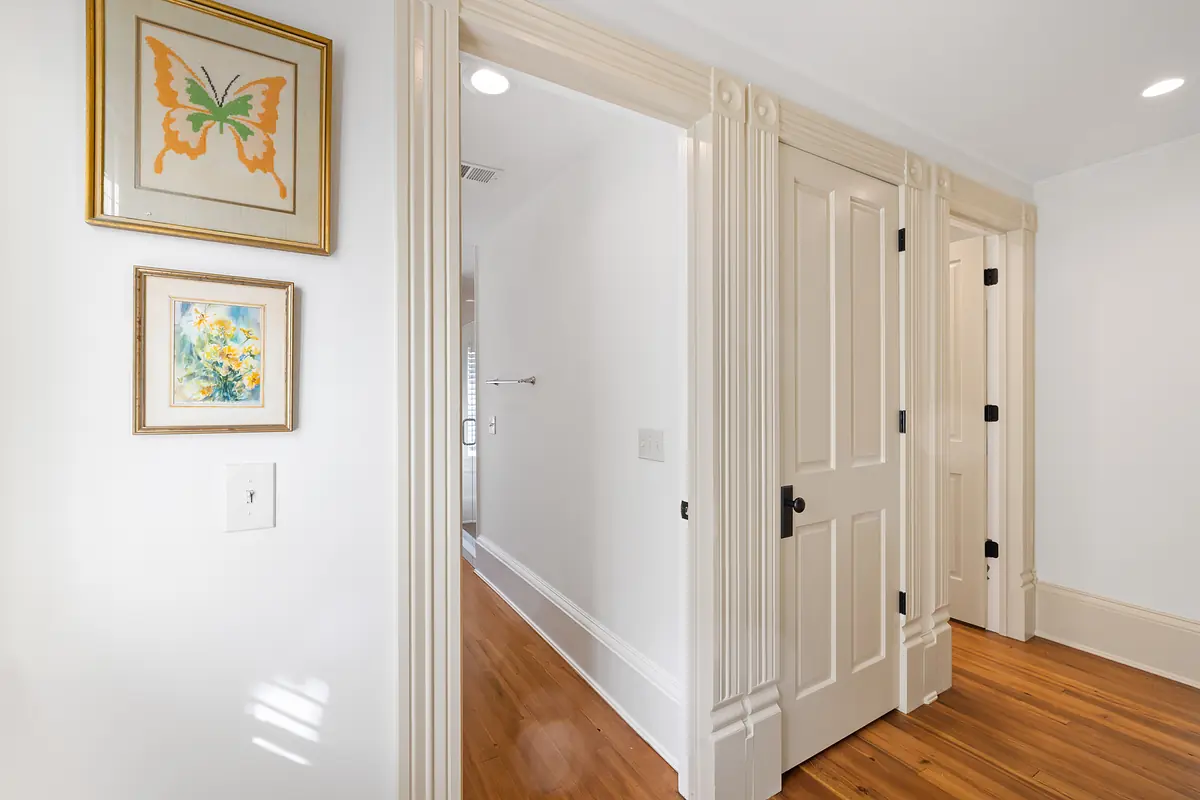 Hallway with white walls, hardwood flooring, framed artwork, and closed doors with black hardware