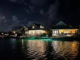 Waterfront property at night with large windows, deck, and outdoor seating.