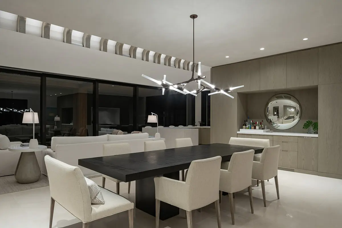 Dining room with black table, white chairs, circular mirror, buffet cabinet, large windows, and modern chandelier
