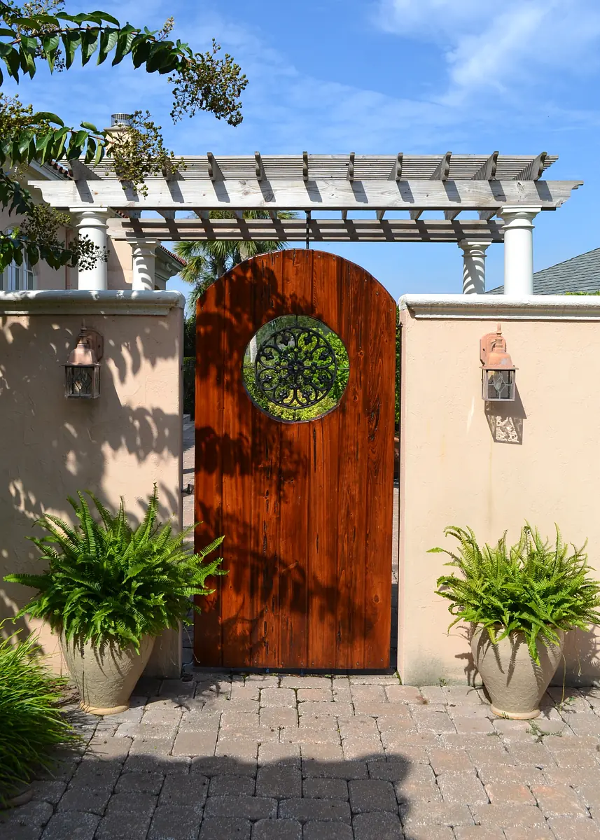 Exterior front area with wooden gate, ferns, stone pathway, and wooden pergola.