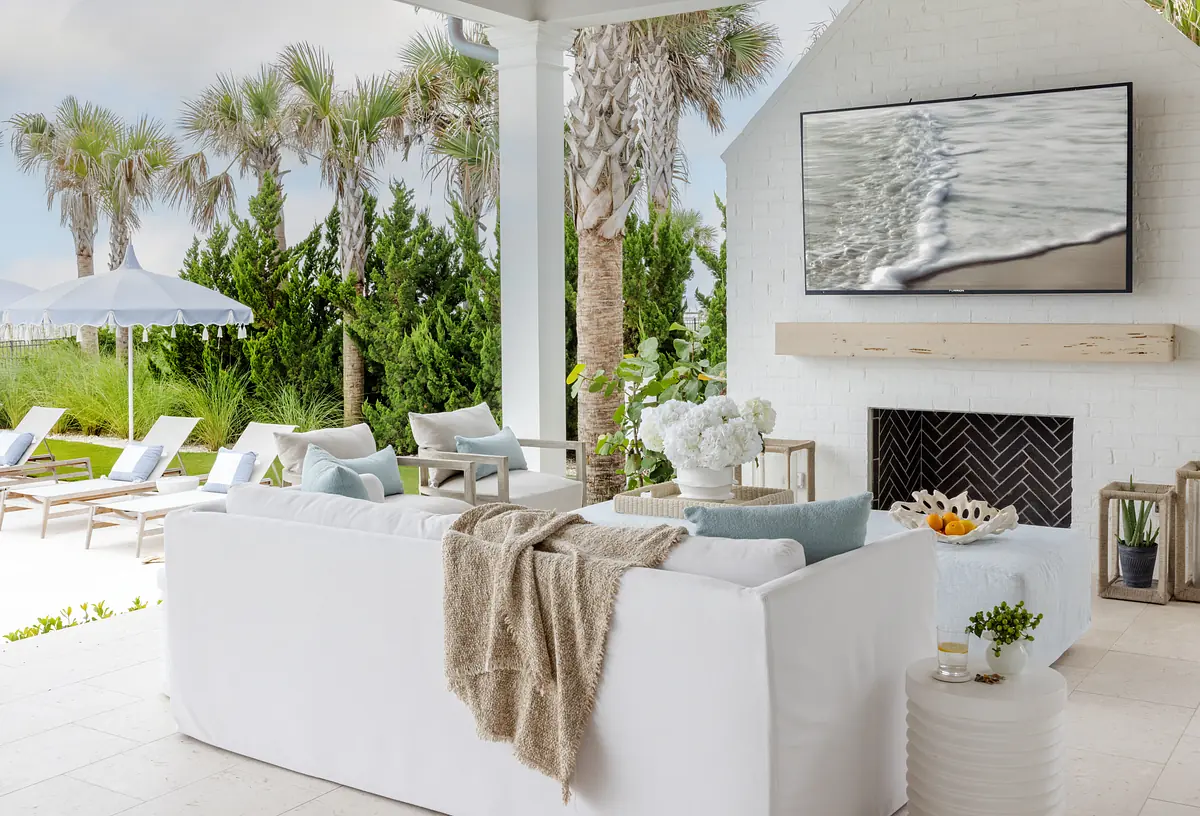Patio with white sofa, wooden coffee table, mounted TV, and palm trees in the background.