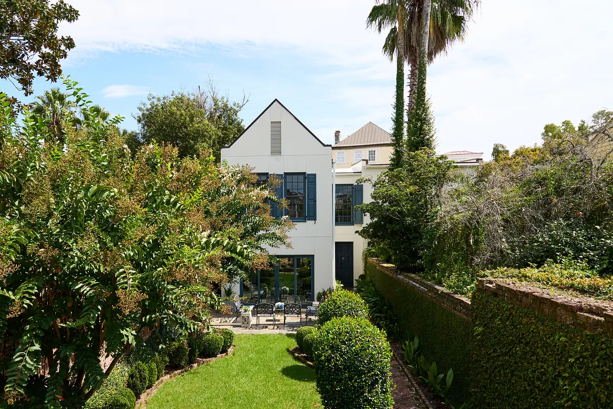 Garden area with grass, hedges, bushes, palm trees, and a two-story house with patio seating