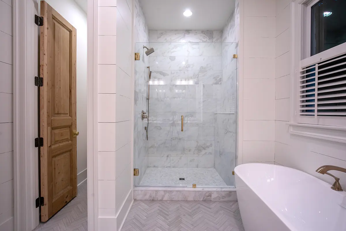 Bathroom with glass shower, freestanding tub, marble walls, and herringbone tiled floor