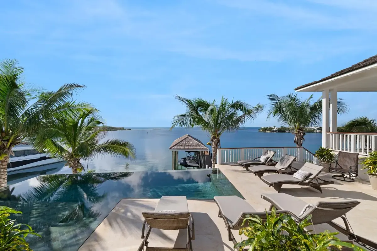 Patio with infinity pool, lounge chairs, palm trees, and gazebo overlooking the ocean.