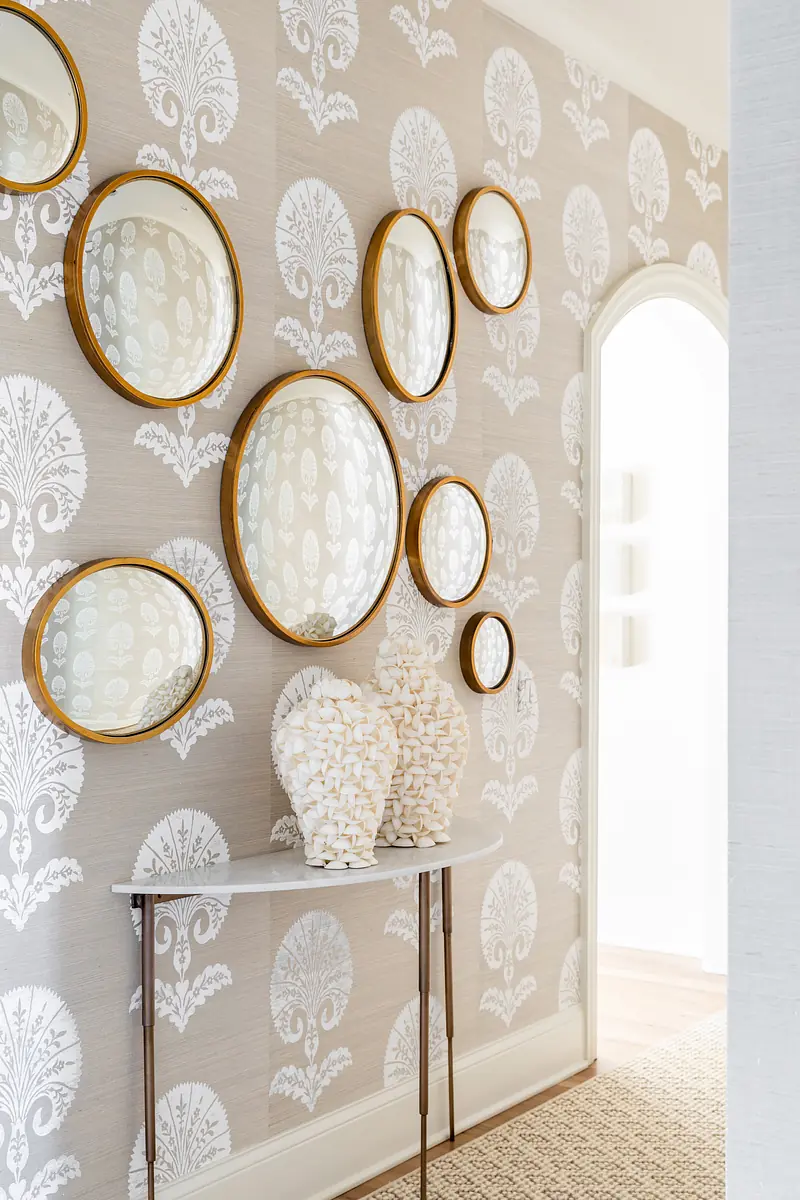 Foyer with console table, round mirrors, and patterned wallpaper.