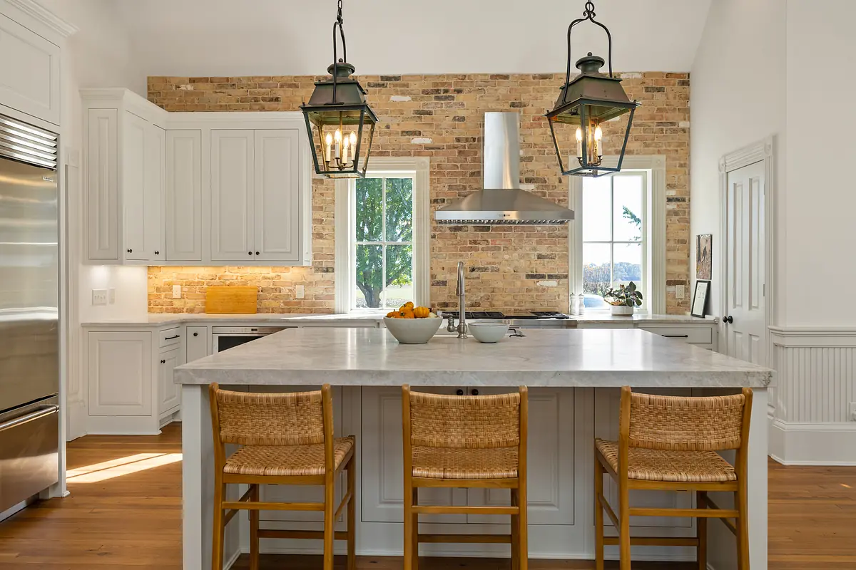 Kitchen with marble island, wicker bar stools, stainless steel appliances, and large windows