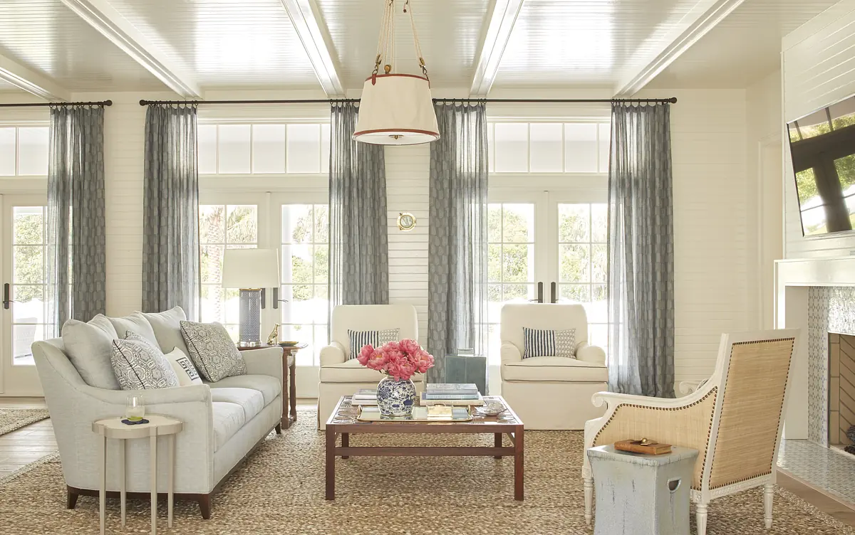 Living room with gray sofa, armchairs, coffee table, area rug, large windows, and a mounted television over a fireplace