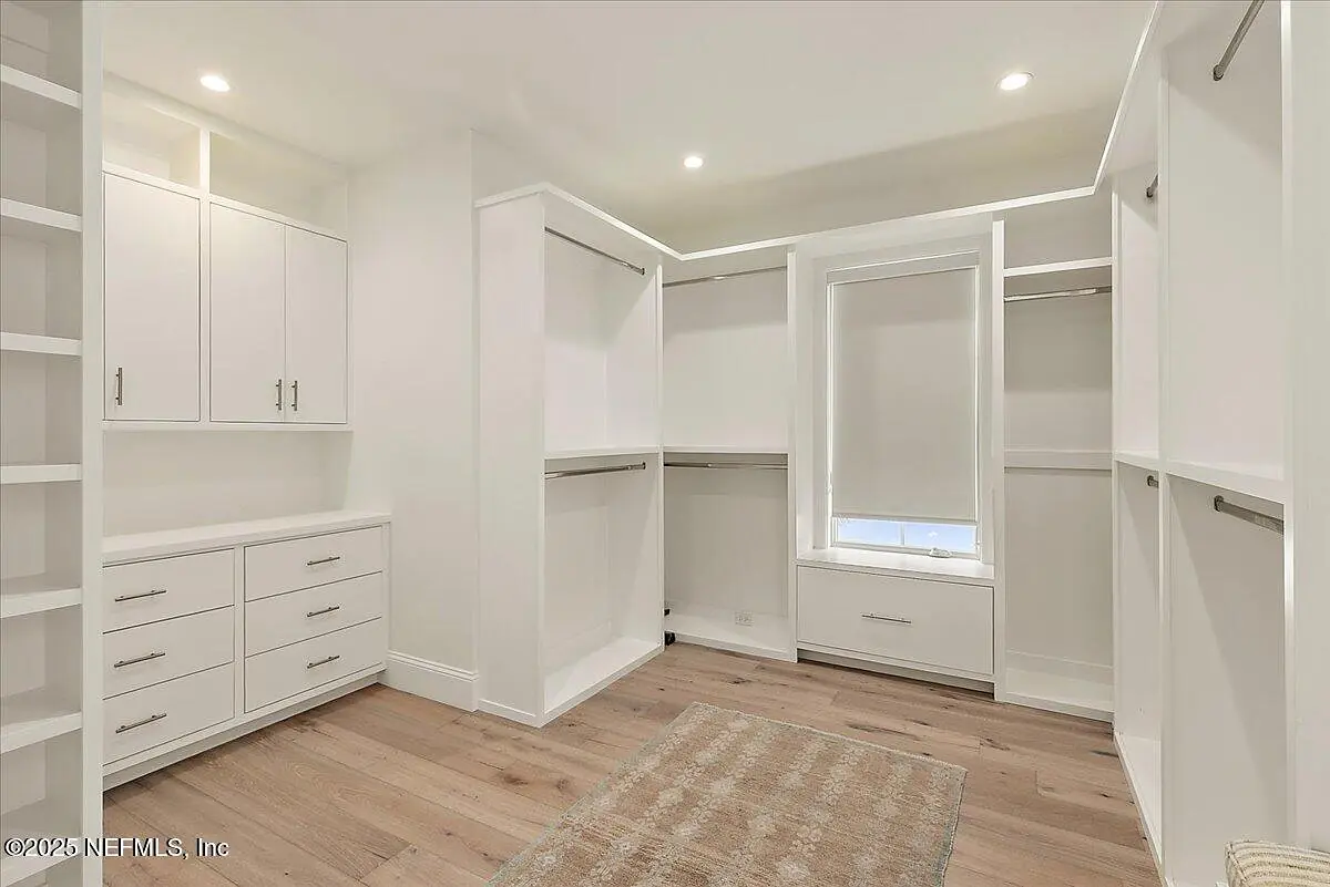 Closet with built-in white cabinetry, shelves, hanging spaces, and natural light from a window.