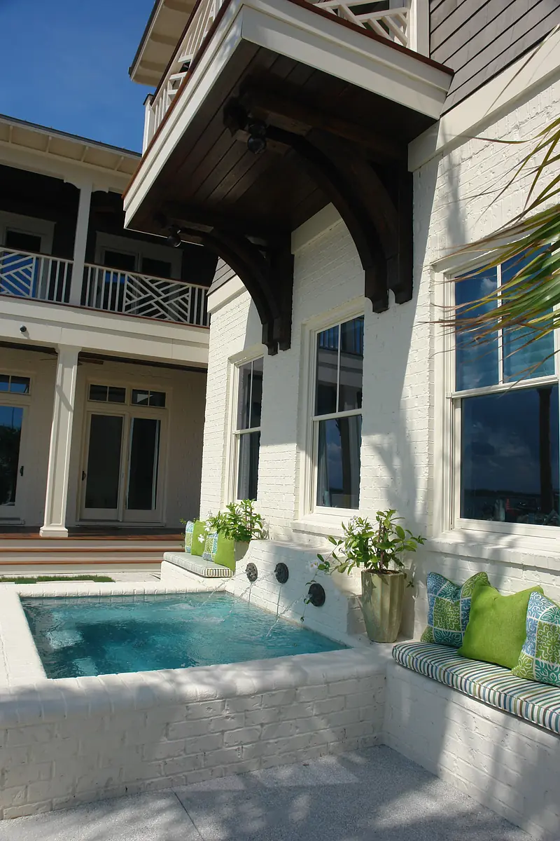Exterior rear area with brick wall, splash pool, plants, and bench with cushions