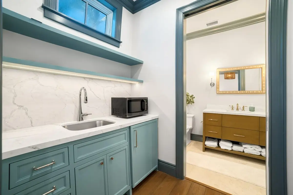 Laundry room with blue cabinetry, sink, microwave, open shelves, and a doorway to a bathroom.