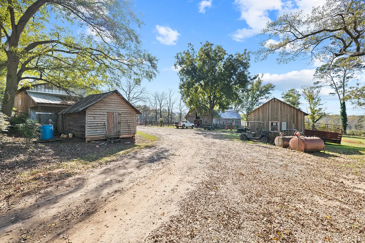 Exterior scene with wooden structures, dirt pathway, trees, equipment, and partly cloudy sky.