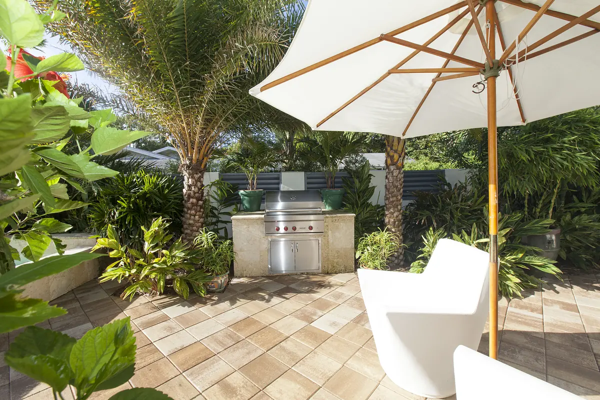 Patio area with stainless steel grill, white umbrella, white chair, and various green plants.