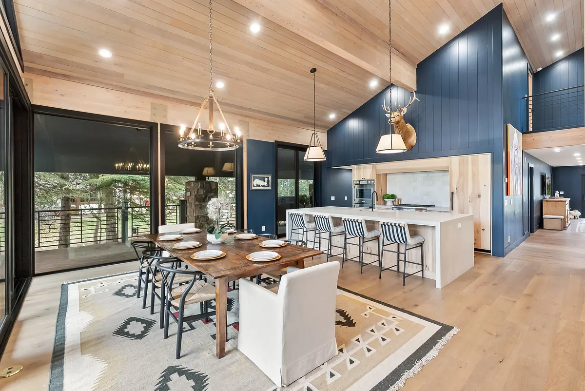 Dining room with wood table, white chairs, rug, bar counter, high stools, and large windows for outdoor views.