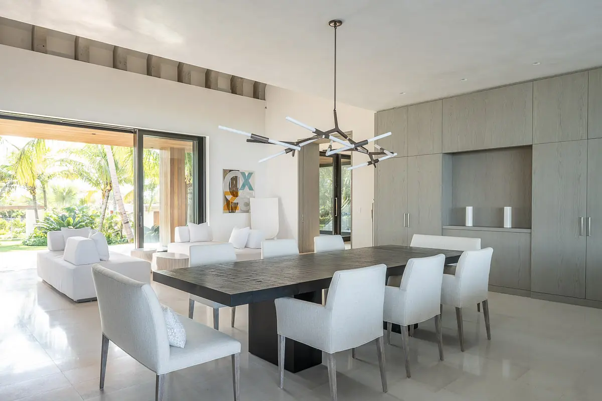 Dining room with wood table, eight white chairs, sliding glass door, built-in cabinetry, and modern chandelier