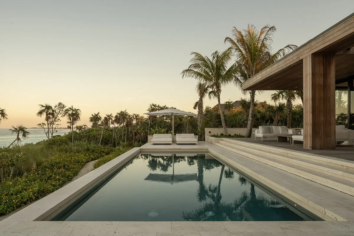 Outdoor space with swimming pool, lounge chairs, umbrella, and lush greenery surrounding a modern structure.