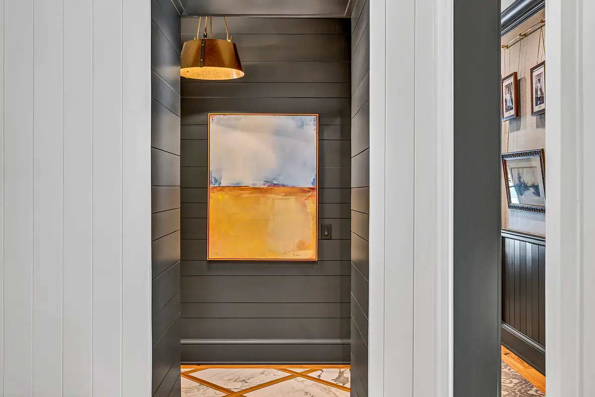 Hallway with gray paneling, abstract painting, patterned tile floor, and pendant light.