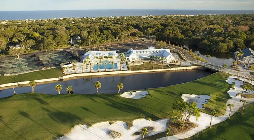 Outdoor landscape with pool, tennis courts, water body, and golf course elements amidst lush greenery.