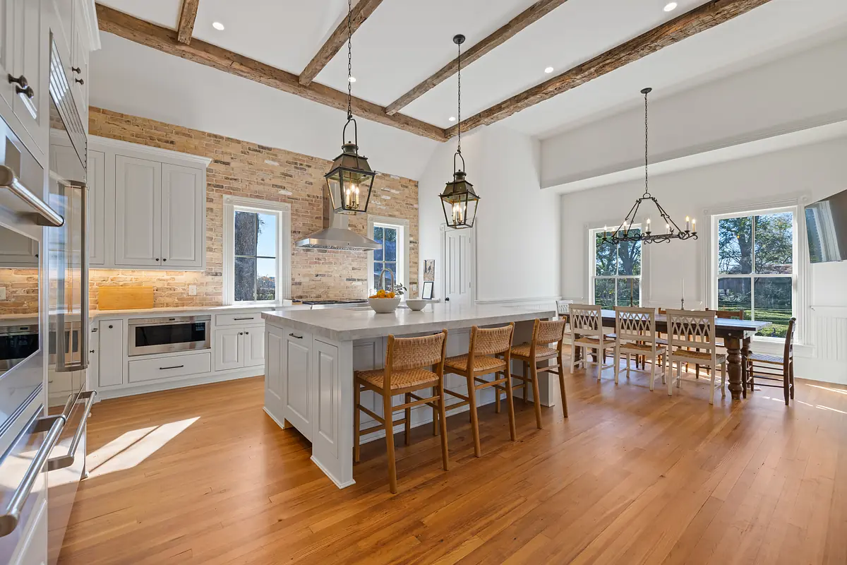 Kitchen with island, bar stools, white cabinetry, wood beams, and a dining table with chairs.