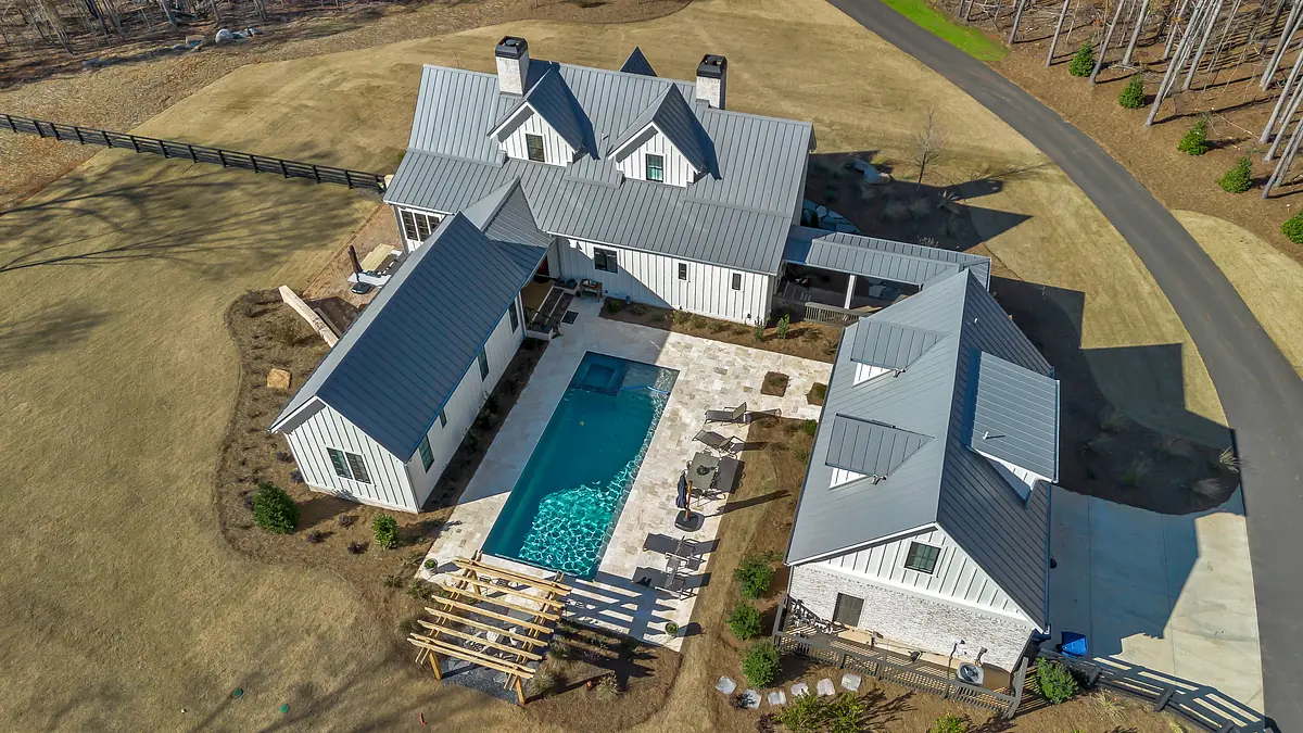 Exterior view of a house with swimming pool, stone patio, and sloped metal roof.