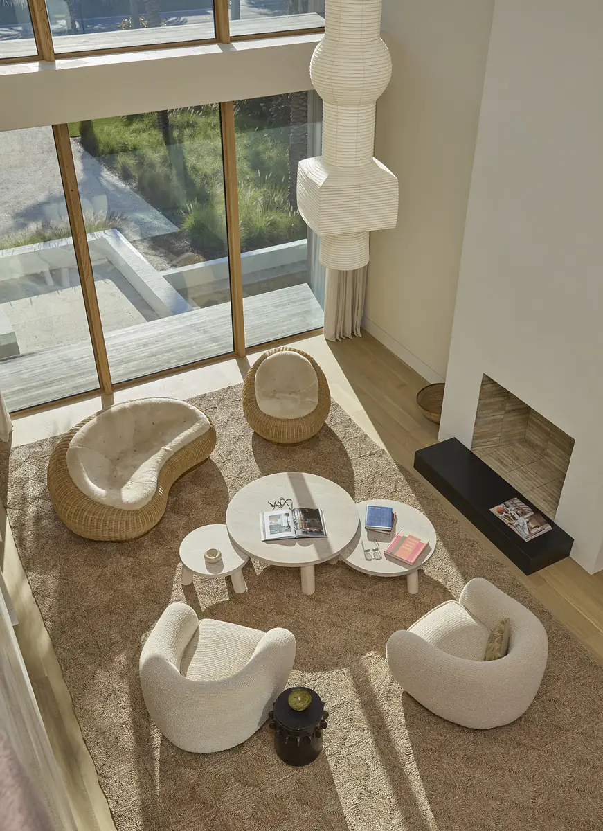 Living room with circular coffee table, cream chairs, curved beige chair, black fireplace, large window, and area rug.