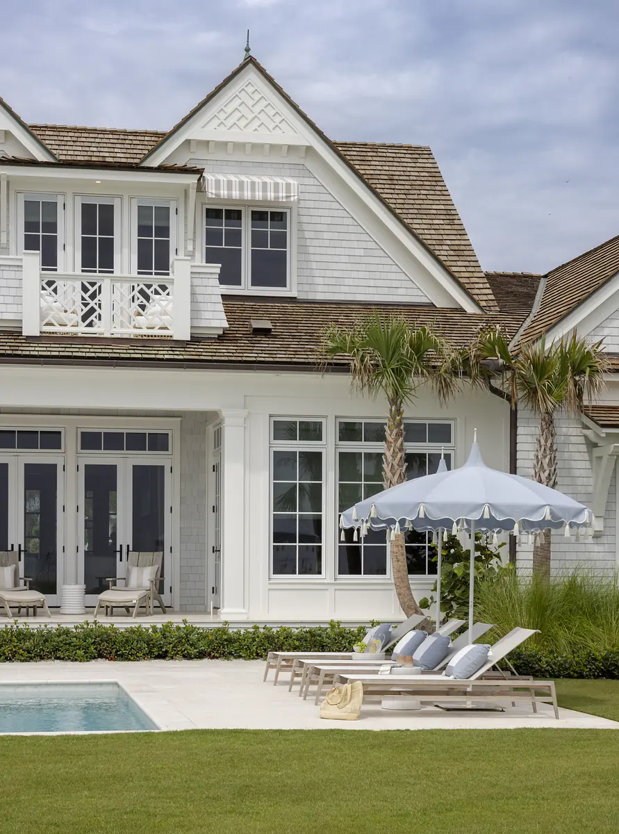 Exterior rear view of a house with pool, loungers, patio umbrella, and landscaped grass.