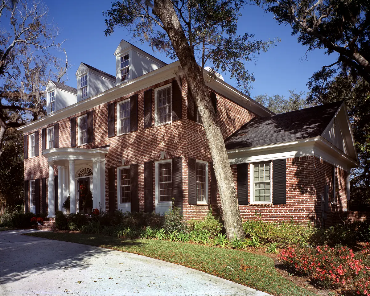 Exterior front of a two-story brick house with white trim, arched front door, and landscaped garden.
