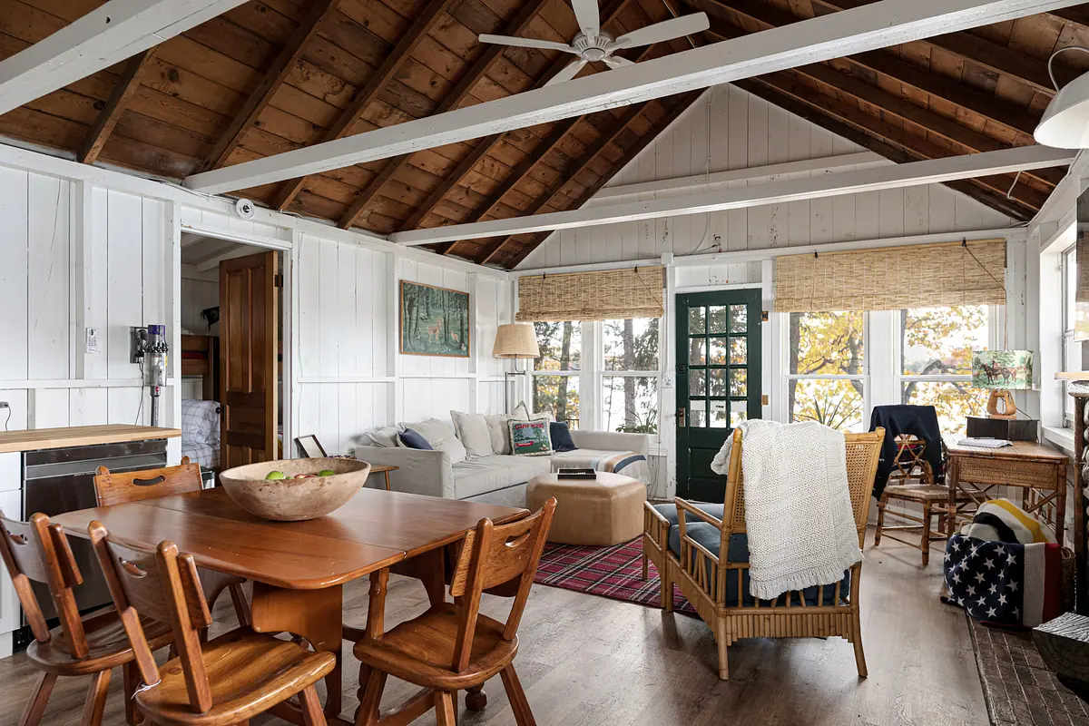 Living room with white sofa, beige armchair, wooden dining table, wicker chair, area rug, and large windows with bamboo shades