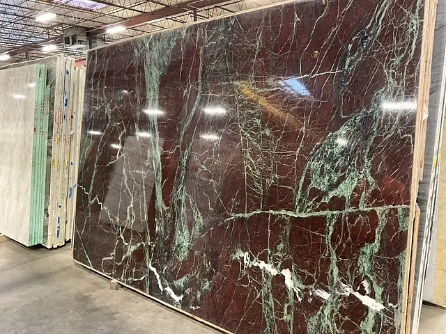 Warehouse displaying large red and green marble slabs with overhead fluorescent lighting.